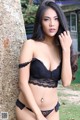 A woman in a black lingerie leaning against a tree.