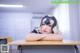 A woman wearing a mask sitting at a desk in a classroom.