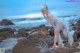 A woman in a white dress standing on a rock by the ocean.