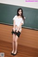 A woman in a white shirt and black skirt posing in front of a blackboard.