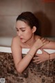 A woman sitting in a bathtub with her hands on her face.