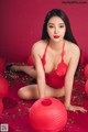 A woman in a red lingerie sitting on a red carpet.