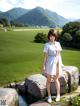 A woman in a white dress standing on a rock by a pond.