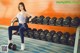 A woman sitting on a bench in a gym with dumbbells.