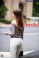 A woman in a gray top and white pants is walking down the street.