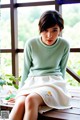 A woman sitting on a wooden bench wearing a green sweater and white skirt.