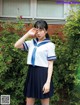 A woman in a school uniform salutes at the camera.