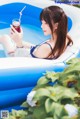 A woman in a blue bikini sitting on an inflatable pool with a drink.