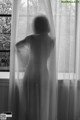 A black and white photo of a woman standing in front of a window.