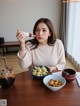 A woman sitting at a table with a bowl of food and a cup of coffee.