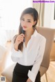 A woman in a white shirt and black skirt sitting on a chair.