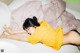 A woman laying on a bed in a yellow shirt.