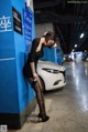 A woman leaning against a blue wall next to a white car.