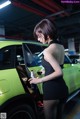 A woman in a black dress standing next to a green car.