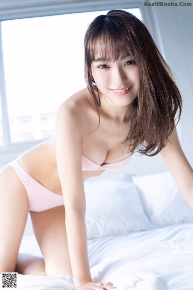 A woman in a pink bikini sitting on a bed.