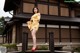 A woman in a yellow kimono standing on a wooden bridge.