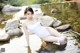 A woman in a white bathing suit sitting on a rock in the water.