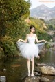 A woman in a white dress standing on a rock by a river.