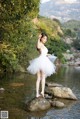 A woman in a white dress standing on a rock in the water.