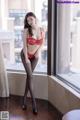 A woman in a red lingerie posing by a window.