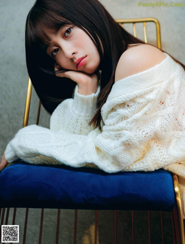A woman sitting on a chair wearing a white sweater.