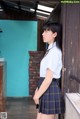 A woman in a school uniform leaning against a wall.