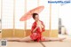 A woman in a red kimono sitting on the floor holding an umbrella.