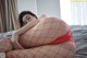 A woman in a red fishnet pantyhose laying on a bed.